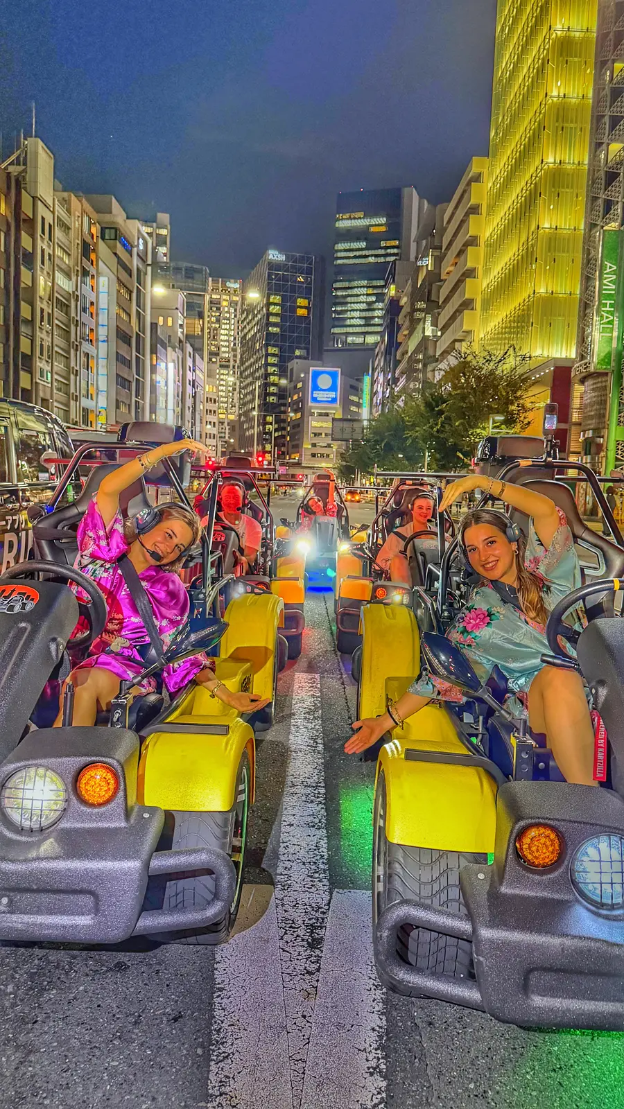 Group of Kira Kira riders in colorful kimono-style robes posing from their go-karts on a wide Tokyo boulevard at night