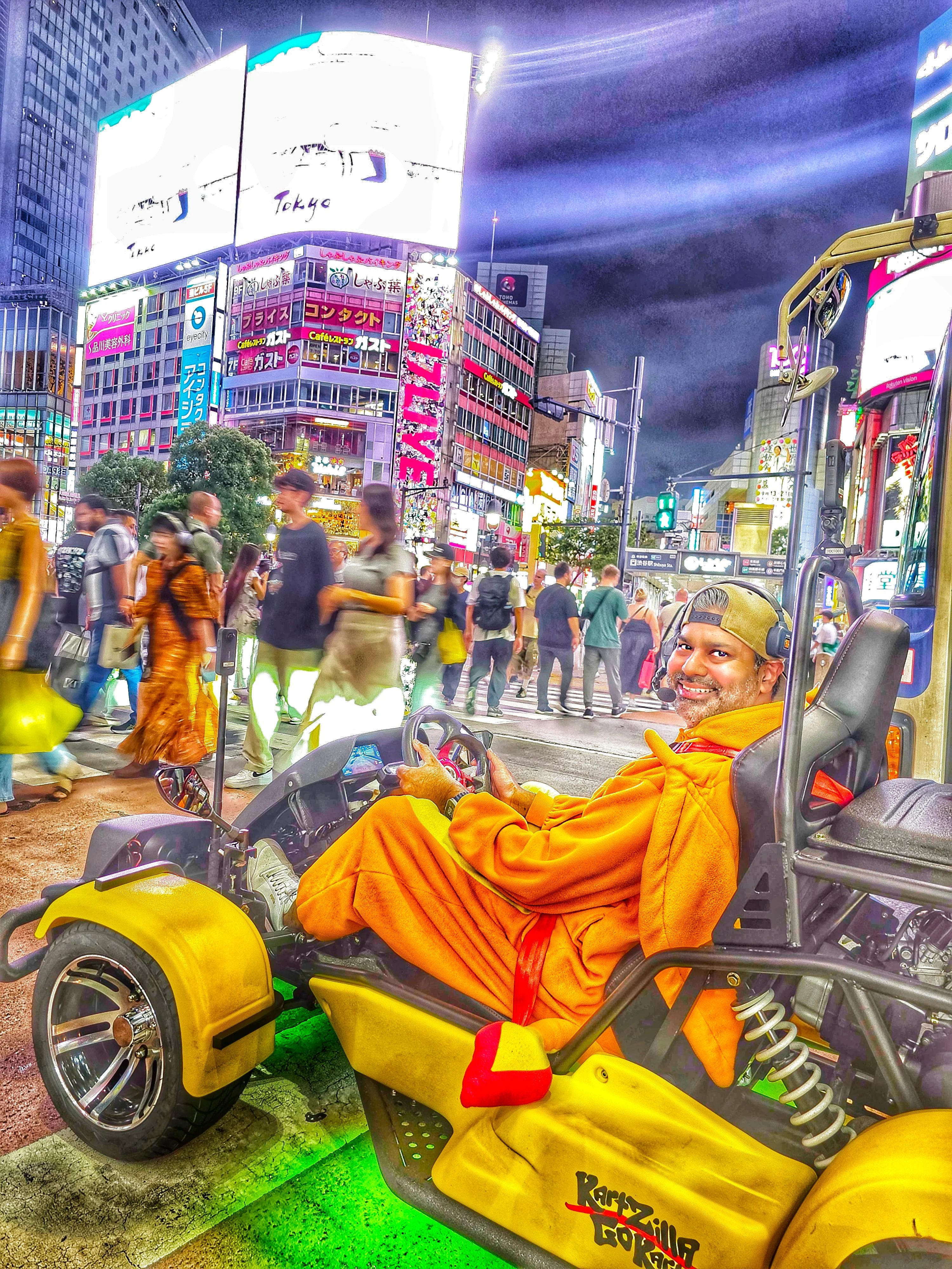 Smiling man in an orange jumpsuit seated in a yellow go-kart with green underglow on a bustling Shibuya street at night, surrounded by neon signs.