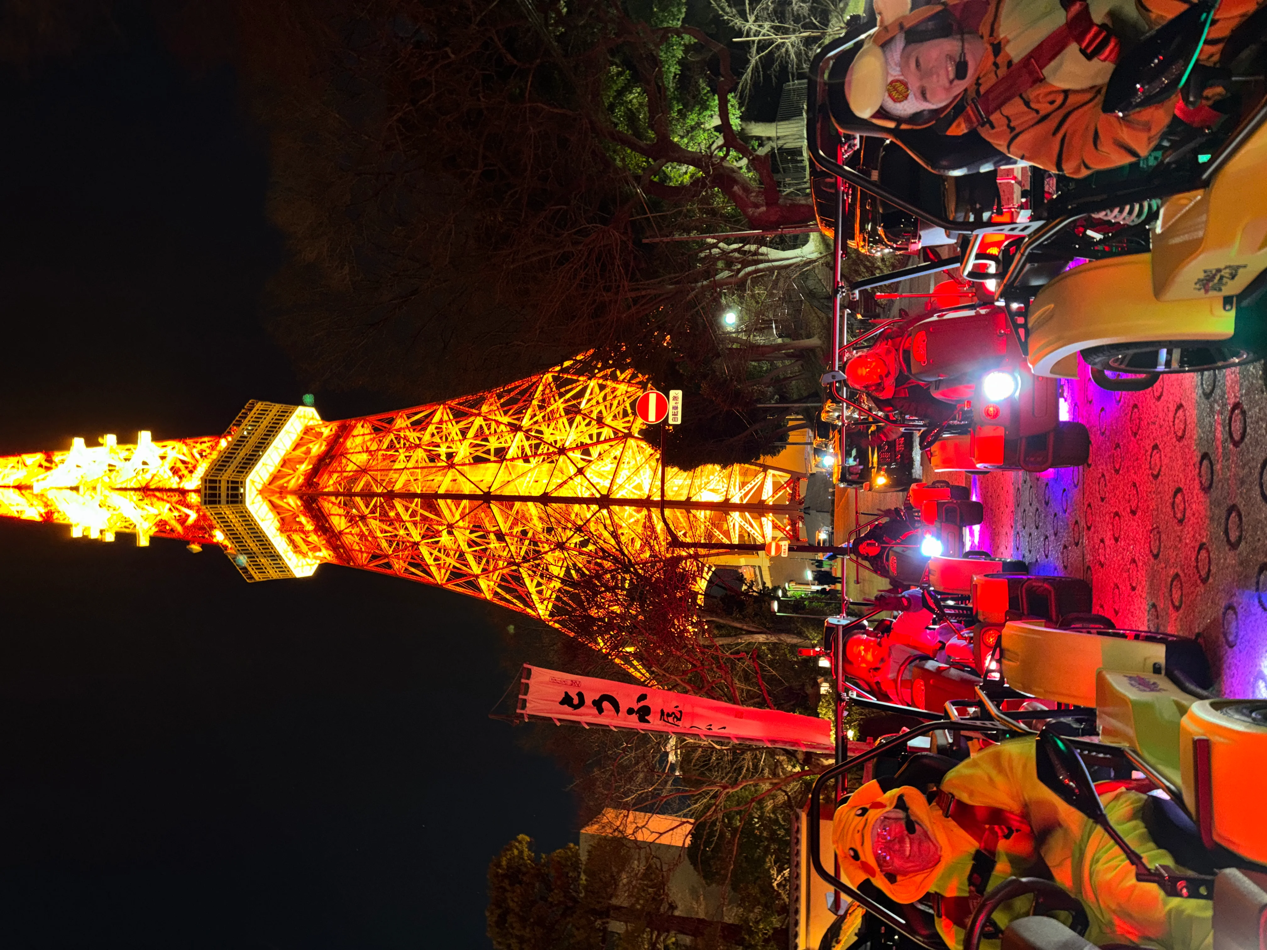 Night scene with the brightly illuminated Tokyo Tower overhead and go-kart riders in Pikachu and tiger costumes on the street below.